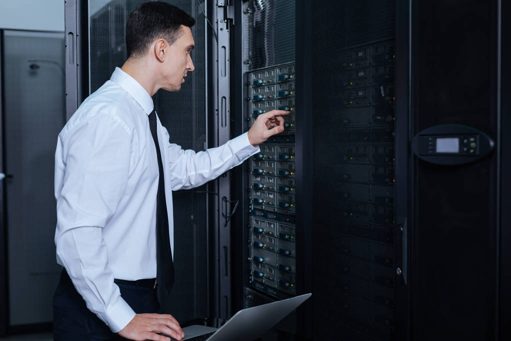 серьезный мужчина с ноутбуком в дата-центре проверяет работу VPS/VDS сервера хостинг-провайдера